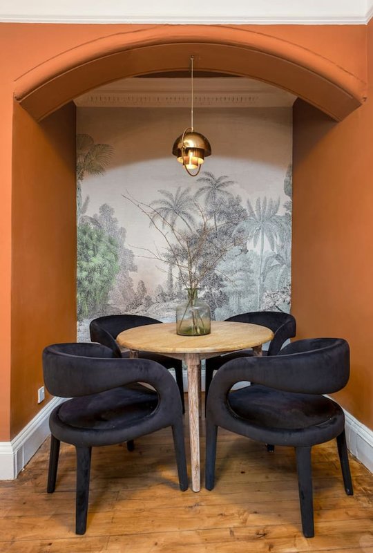 Intimate dining alcove with round wooden table, black upholstered chairs, pendant lamp, and botanical mural
