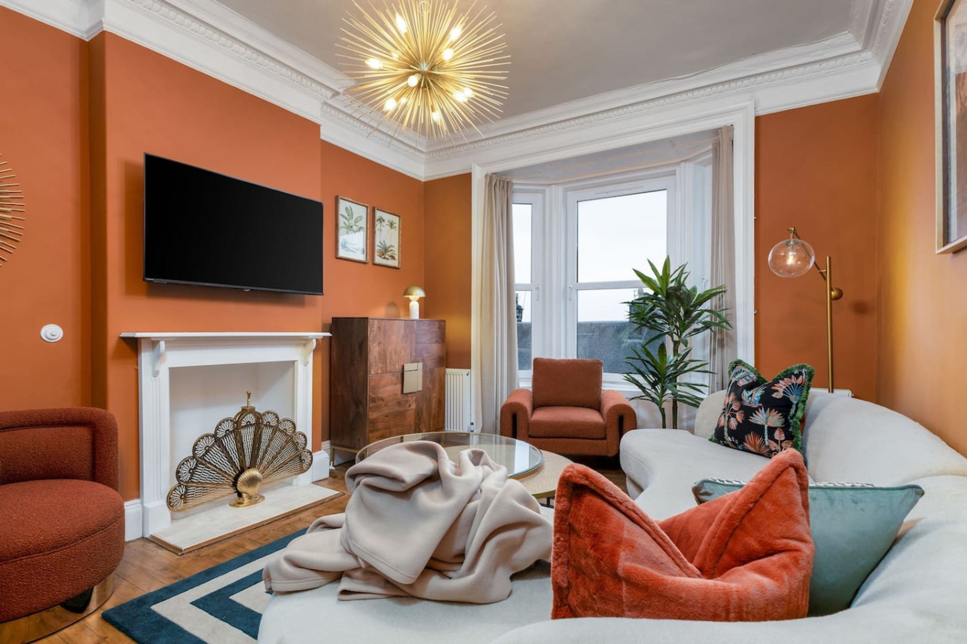 Bright living room with orange walls, fireplace, TV, sofa and armchairs with cushions