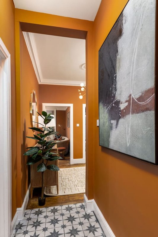 Bright orange hallway with patterned floor, potted plant, and framed artwork on wall