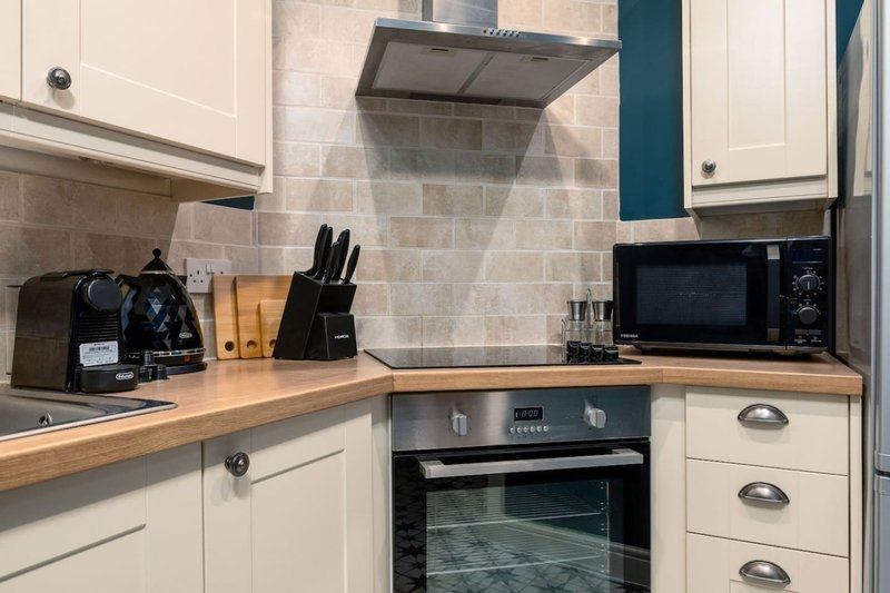 Modern kitchen with cream cabinetry, wooden countertop, stainless steel appliances and teal accent wall
