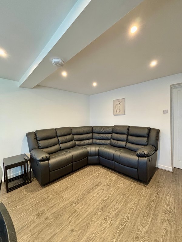 Modern living room with black leather corner sofa, wooden floor and recessed ceiling lights