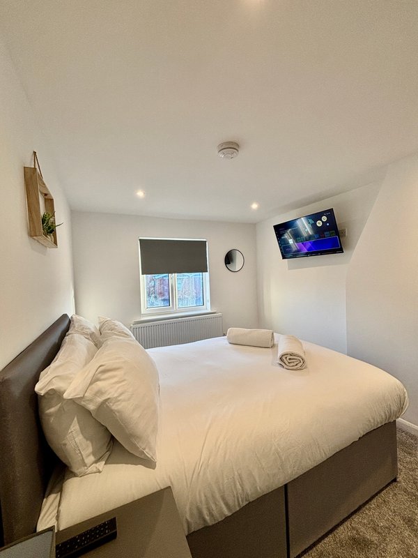 Compact bedroom with double bed, wall-mounted TV, window with blinds and radiator