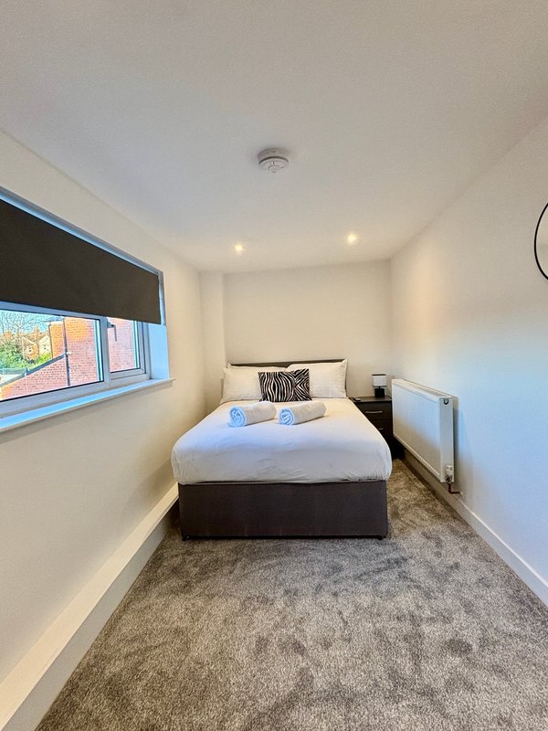 Compact bedroom with double bed, grey carpet, window with blind and bedside table