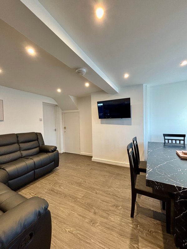 Open-plan living room with black leather recliners, wall-mounted TV, dining table and wooden flooring