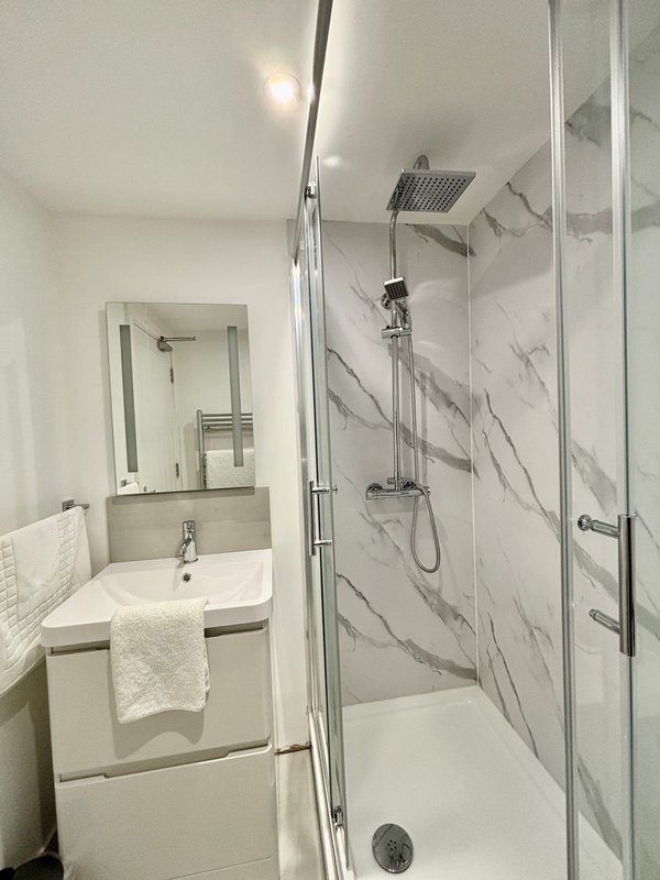 Modern bathroom with white sink, mirror, towel rail and marble-tiled shower enclosure