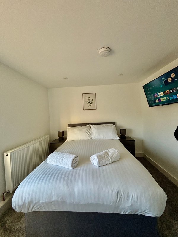 Bedroom with double bed, white bedding, wooden nightstands, wall-mounted TV and framed artwork