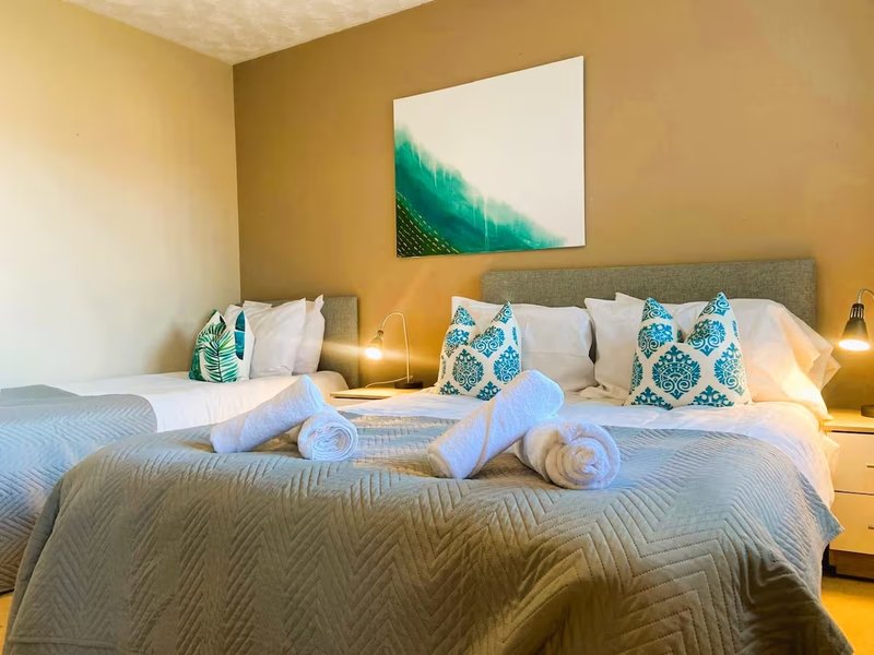 Bedroom with double bed, rolled towels, patterned cushions, bedside lamps and wall art