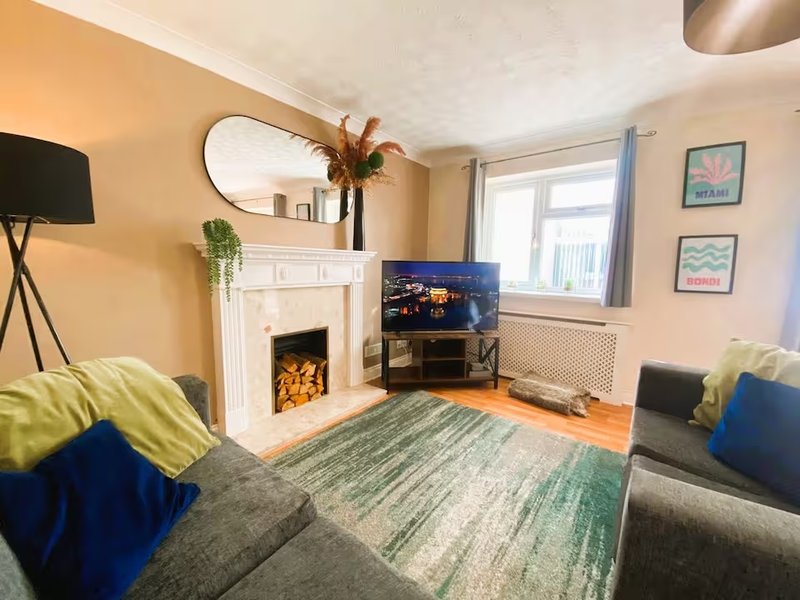 Living room with fireplace, grey sofa, blue and green cushions, TV, and windows