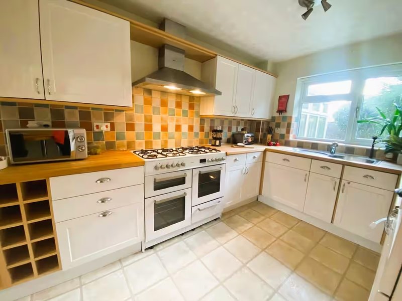Kitchen with white cabinetry, orange and cream checkered backsplash, wooden countertop and double oven