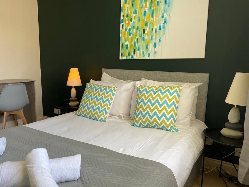 Bedroom with grey upholstered bed, white bedding, patterned cushions, and dark green accent wall
