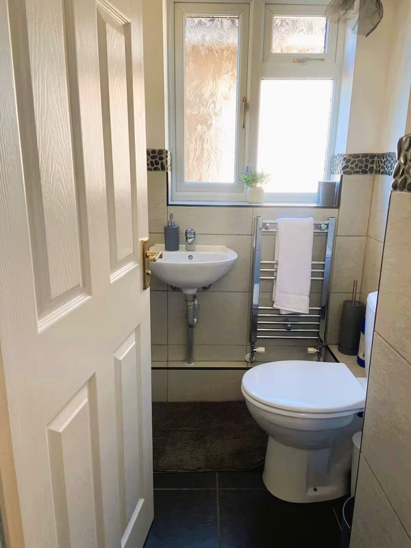 Small bathroom with toilet, wall-mounted sink, towel rail and window