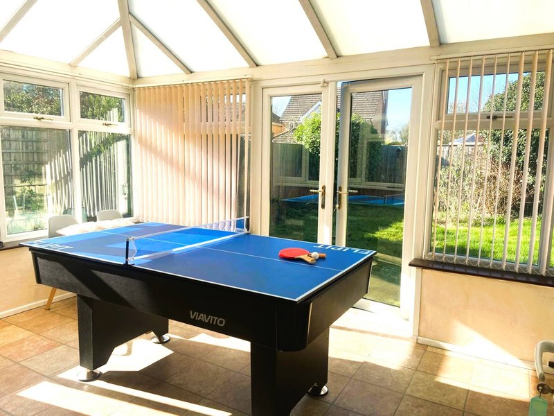 Bright conservatory with ping pong table, garden views through glass doors and windows