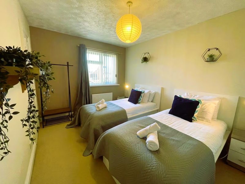 Twin bedroom with two single beds, yellow walls, pendant light, and window with curtains