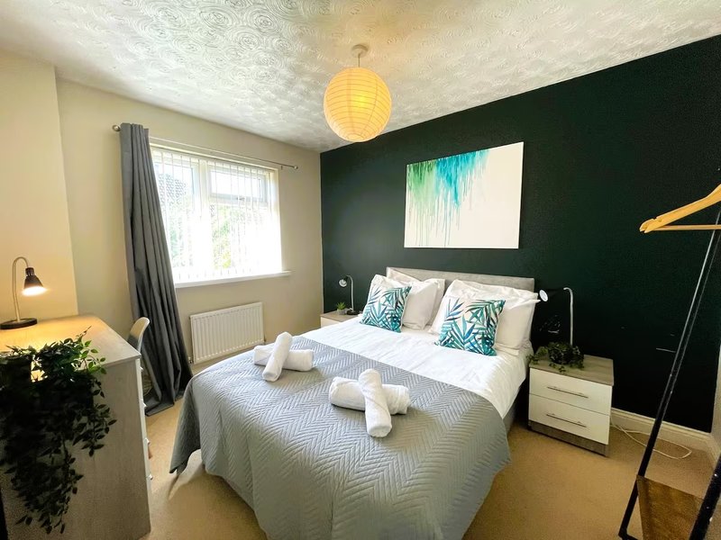Modern bedroom with double bed, white bedding, dark green accent wall and pendant light