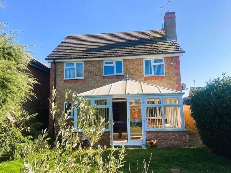 Brick house with conservatory, front garden with shrubs and lawn