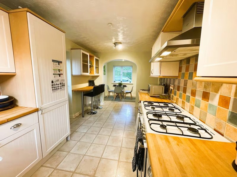 Galley kitchen with gas cooker, wooden worktops, cream cabinets and yellow tile splashback
