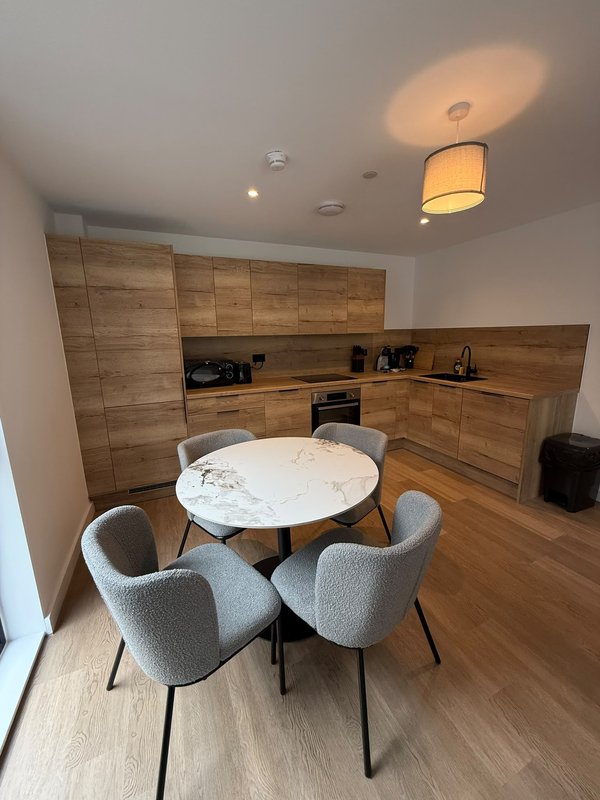 Modern kitchen and dining area with wooden cabinetry, round white table, and grey upholstered chairs