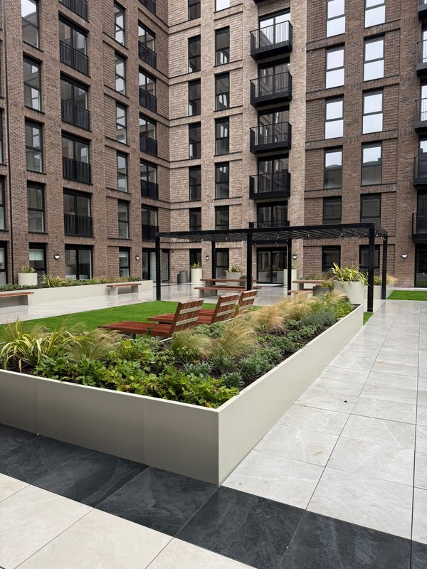 Modern courtyard with planted beds, seating area, and surrounding brick apartment buildings