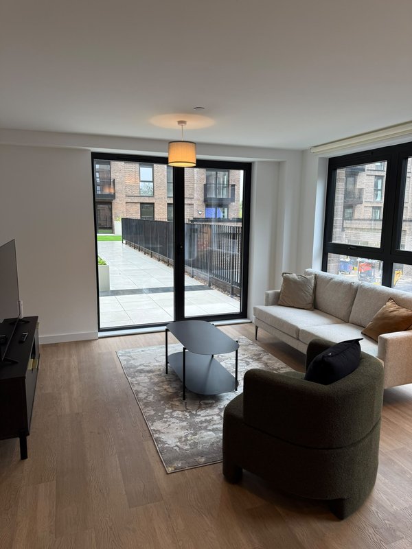 Modern living room with grey armchair, beige sofa, wooden flooring and glass doors to balcony