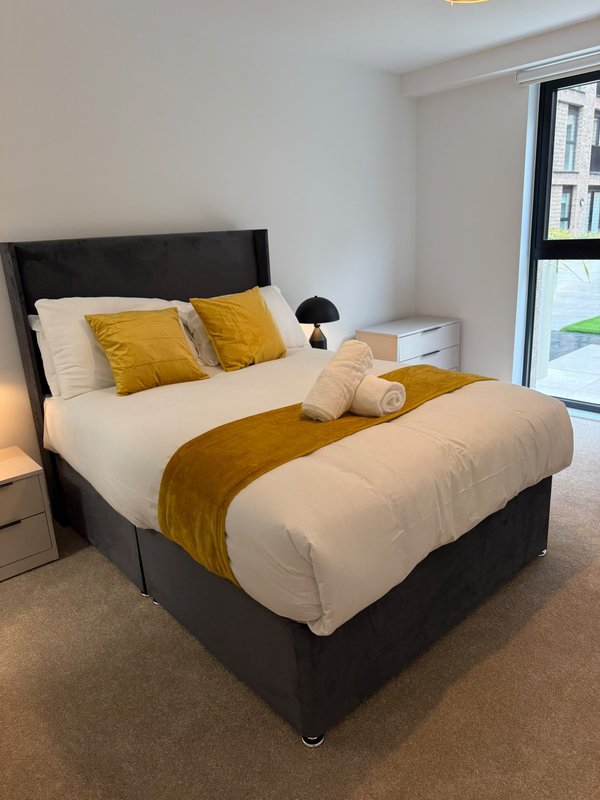 Modern bedroom with black bed frame, white bedding, yellow accent pillows and throw, bedside lamp