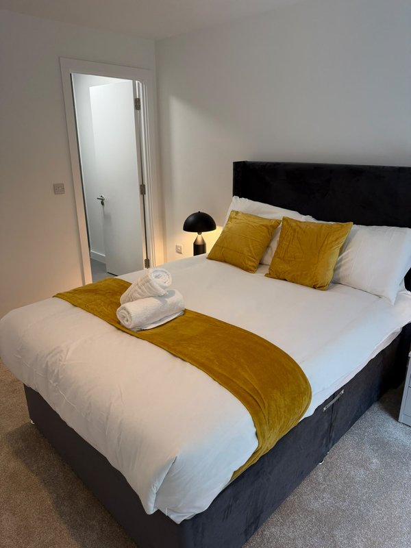 Modern bedroom with black bed frame, white bedding, gold-yellow cushions and throws