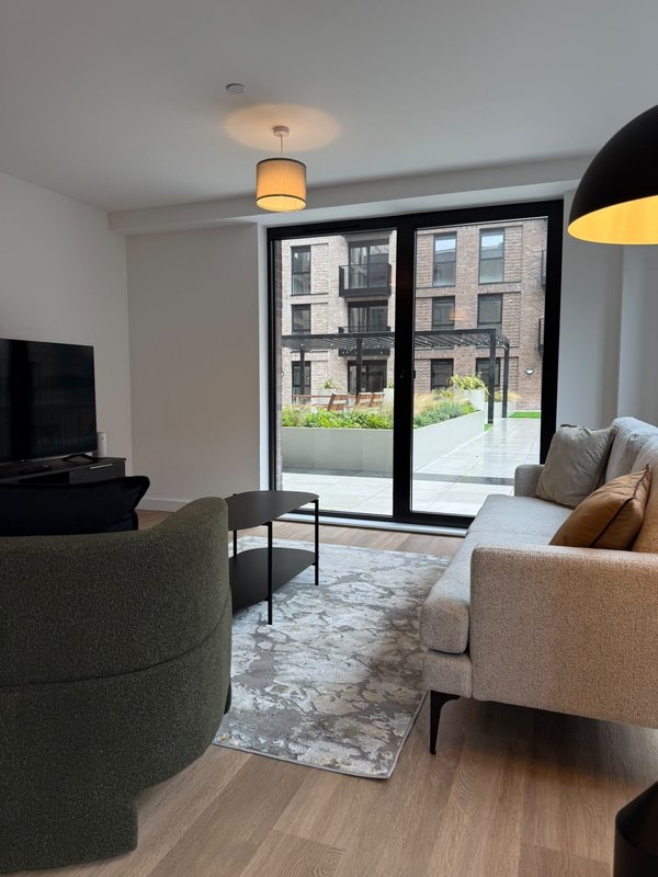 Modern living room with grey armchair, cream sofa, TV, pendant light and glass doors to courtyard