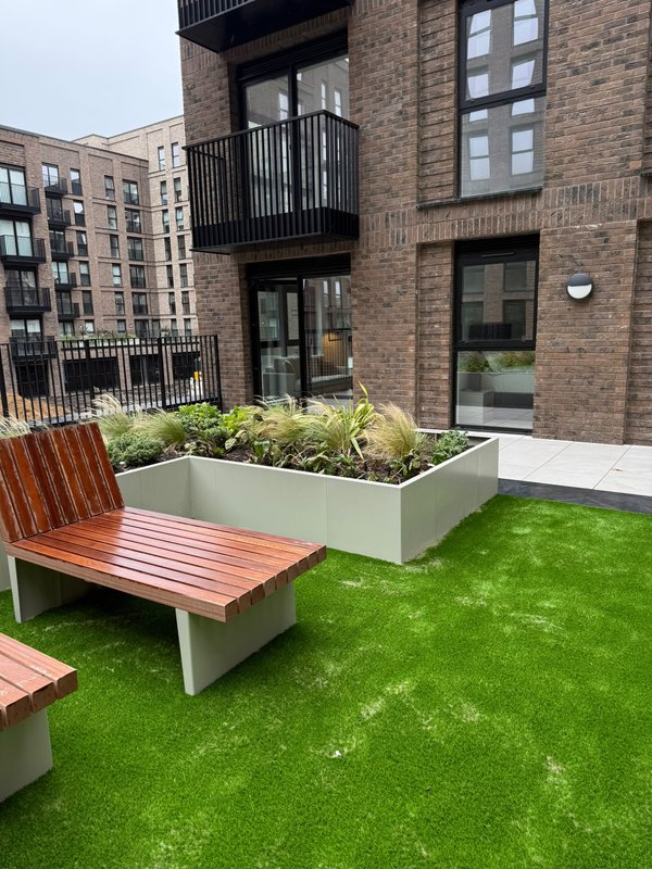 Modern brick building exterior with terrace, artificial grass, wooden bench seating and planters