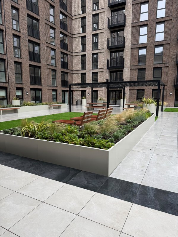 Modern apartment building courtyard with landscaped garden beds and paved seating area