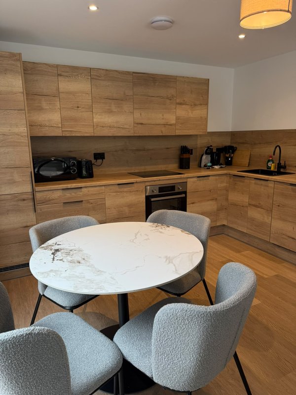 Modern kitchen and dining area with wooden cabinetry, marble table, and grey chairs