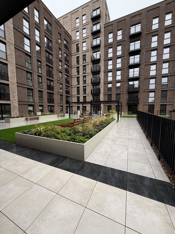 Communal courtyard with paved seating area, planted beds and brick apartment buildings
