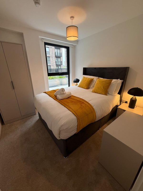 Modern bedroom with double bed, yellow cushions, pendant light and city window view