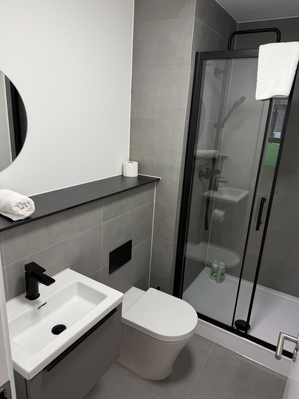 Modern bathroom with white toilet, wall-mounted sink, shower enclosure and grey tile walls