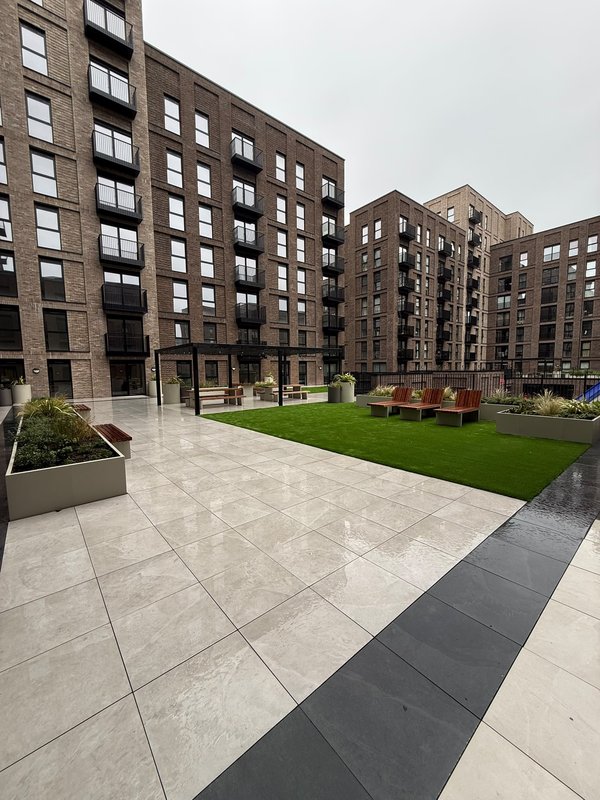 Modern apartment building courtyard with paved plaza, green lawn, and seating areas