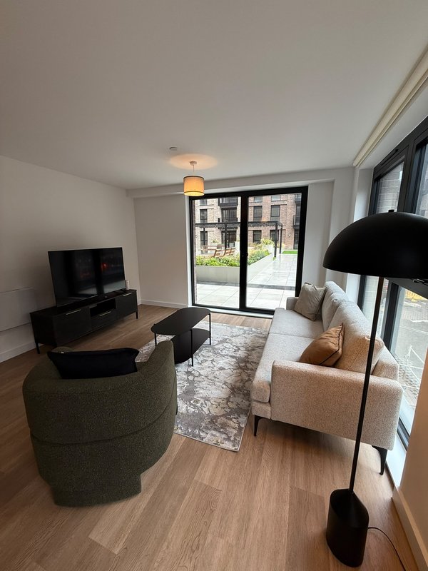 Modern living room with cream sofa, round green ottoman, TV unit and large patio doors with garden view