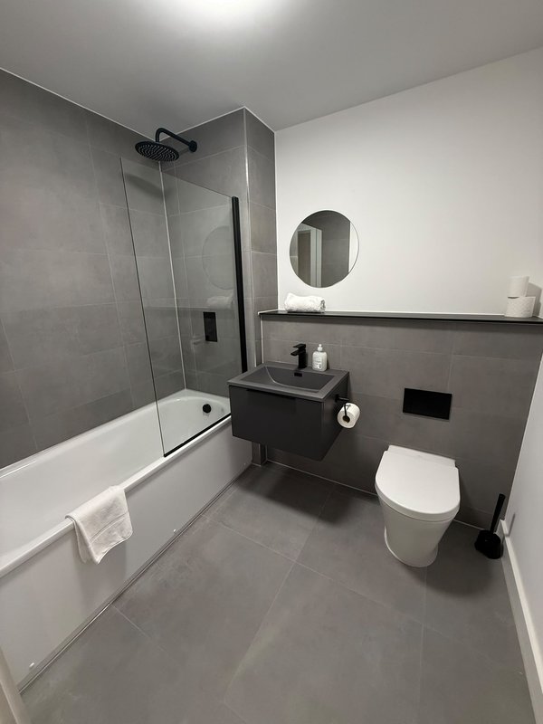 Modern bathroom with walk-in shower, vanity sink, toilet and round mirror