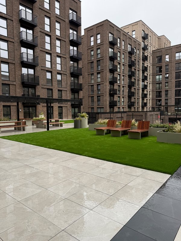 Modern apartment building courtyard with green lawn, paved seating area and red chairs