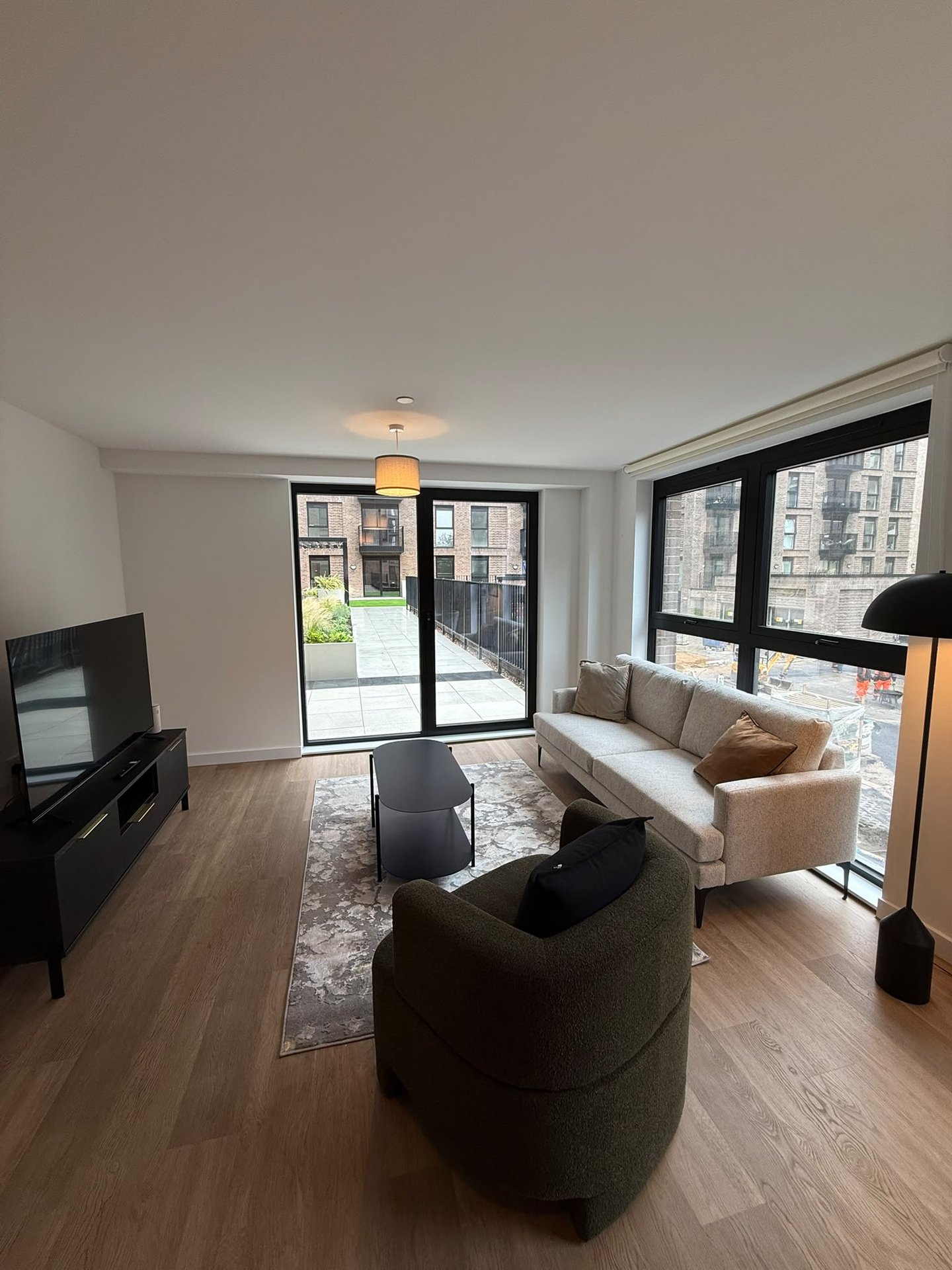 Modern living room with curved seating, wooden flooring, TV unit and large windows overlooking city