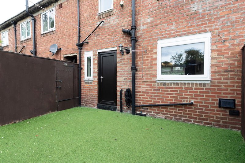 Brick townhouse exterior with paved courtyard, green artificial turf, and black door