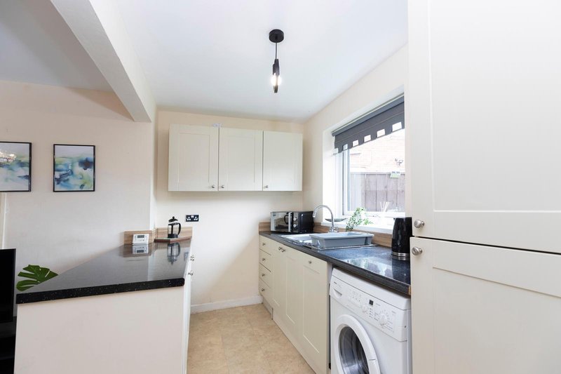 Modern kitchen with cream cabinets, black countertops, washing machine and window