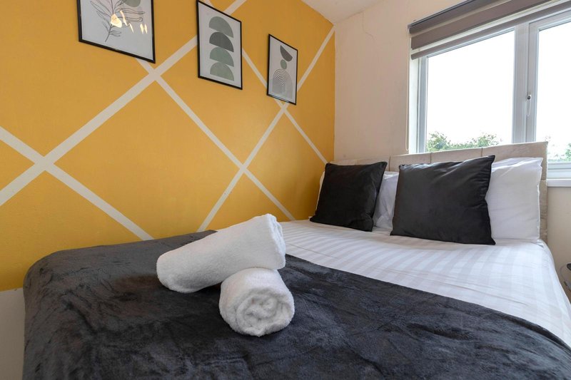 Bedroom with yellow geometric wall, double bed, black duvet, pillows and rolled towels