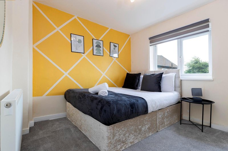Modern bedroom with yellow geometric accent wall, double bed, black pillows and white bedding