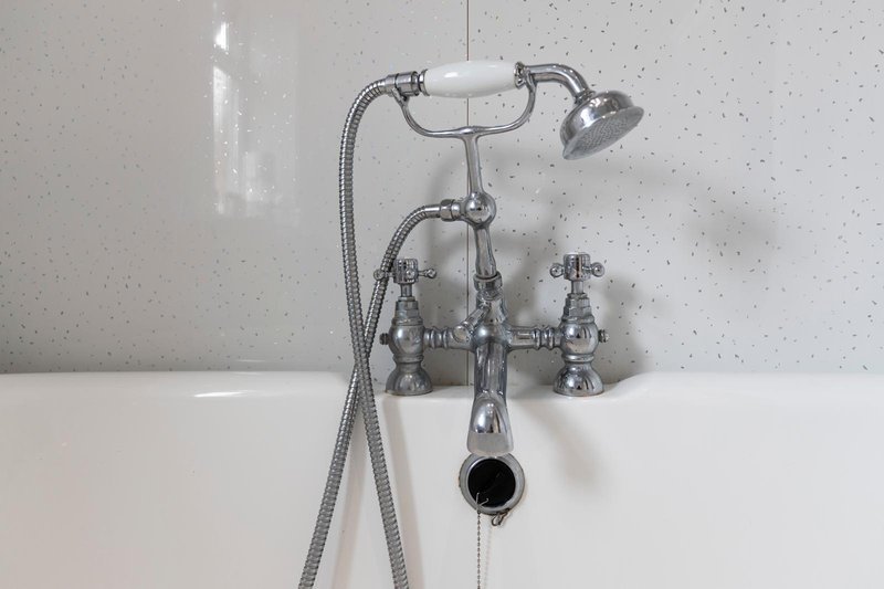 Traditional chrome bath tap and shower head mounted on white speckled bathroom wall