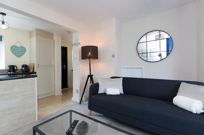 Modern open-plan living room with black sofa, kitchenette, round mirror and pendant lighting