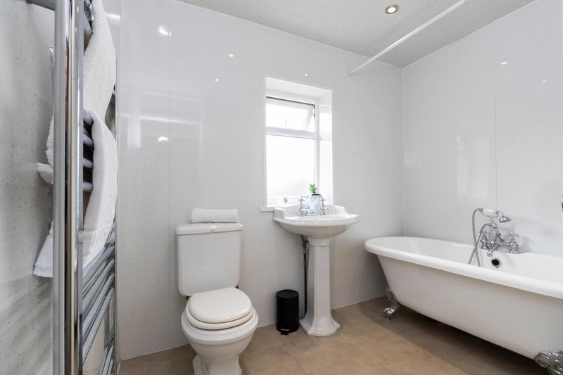 Bright modern bathroom with freestanding bathtub, pedestal sink, toilet, and heated towel rail