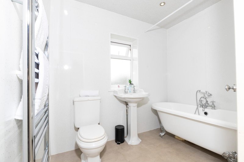 Clean bathroom with white suite, pedestal sink, freestanding bathtub and heated towel rail