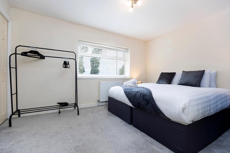 Bright bedroom with double bed, black pillows, garment rail and window with blinds