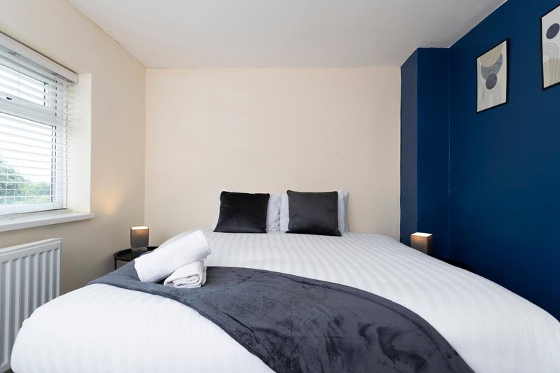 Bedroom with double bed, white bedding, dark blue accent wall and window