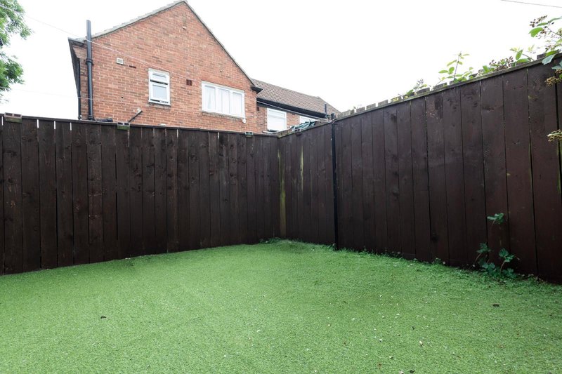 Brick house with dark wooden fence and well-maintained green garden lawn