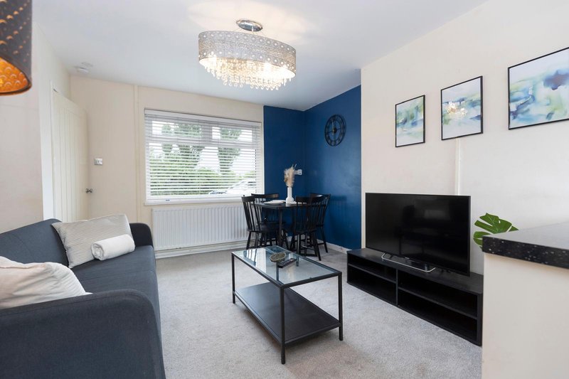 Modern living room with blue accent wall, gray sofa, flat-screen TV, and dining table