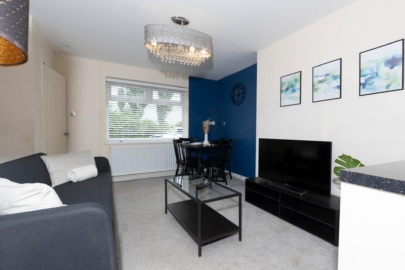 Modern living room with grey sofa, dining area, TV, and blue accent wall